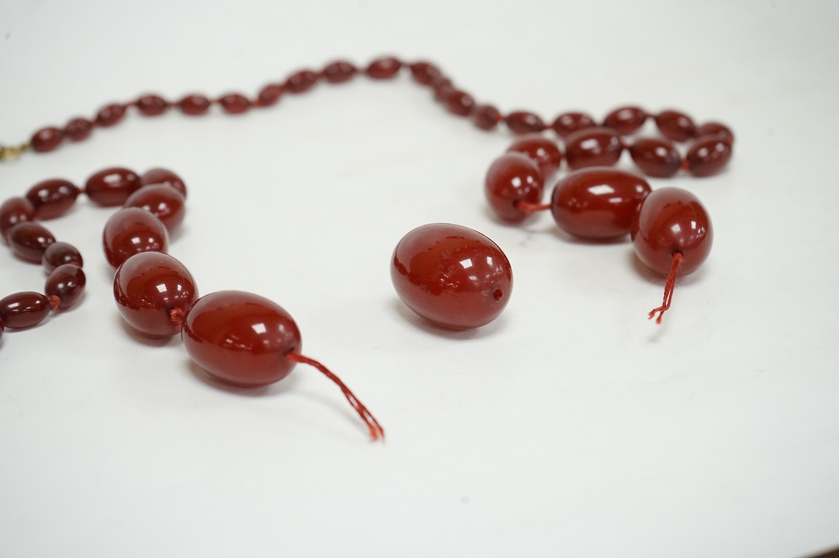 A single strand graduated simulated oval cherry amber bead necklace, string broken, gross weight 73 grams.